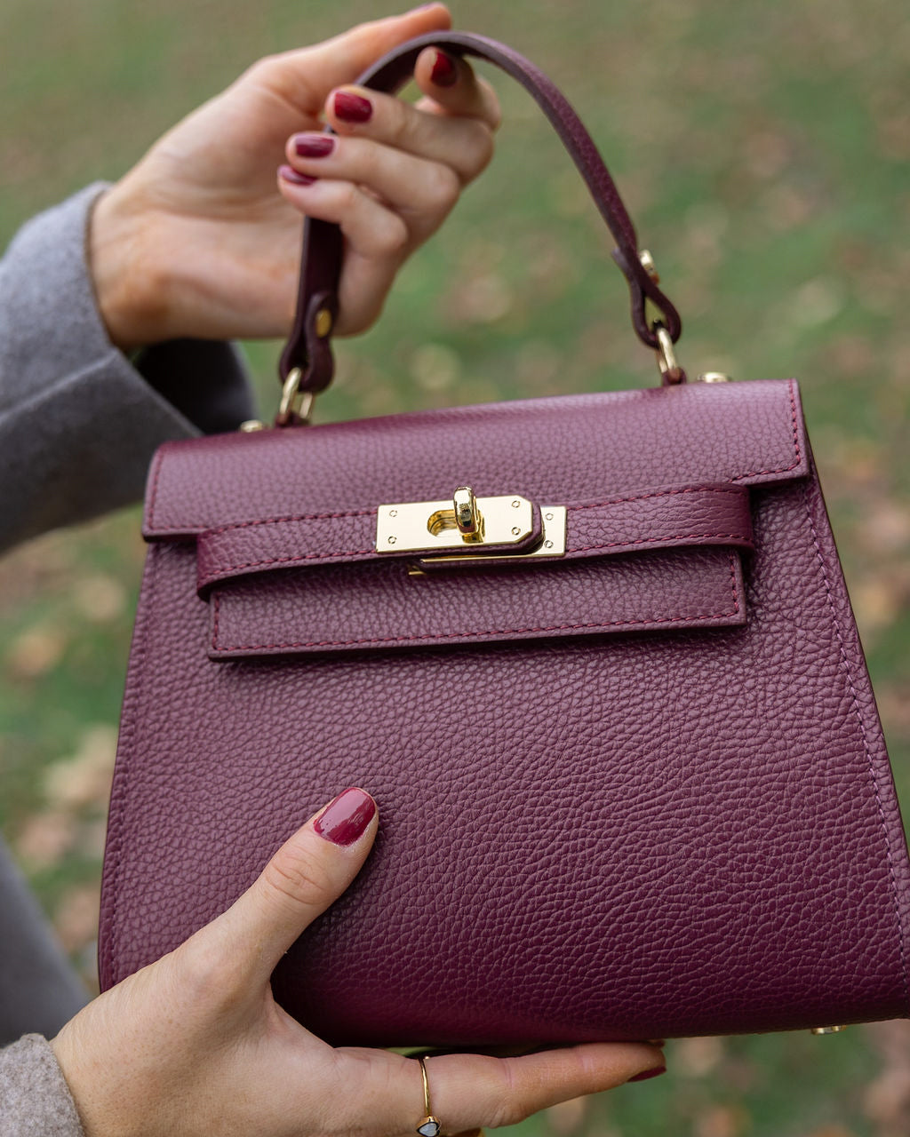 Burgundy handbag held by a person with a blurred green background