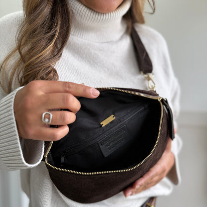 Woman holding a brown leather bag with a gold zipper.