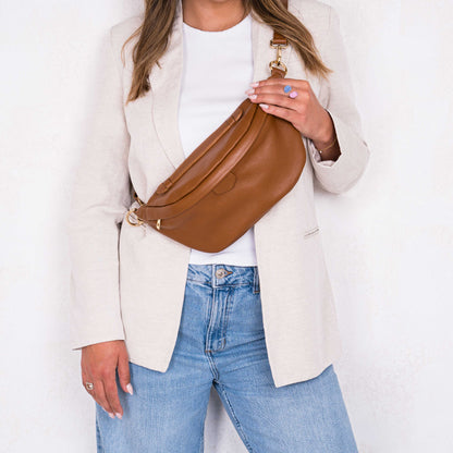 lady wearing cream jacket and jean holding a olivia and gray tan leather bumbag 