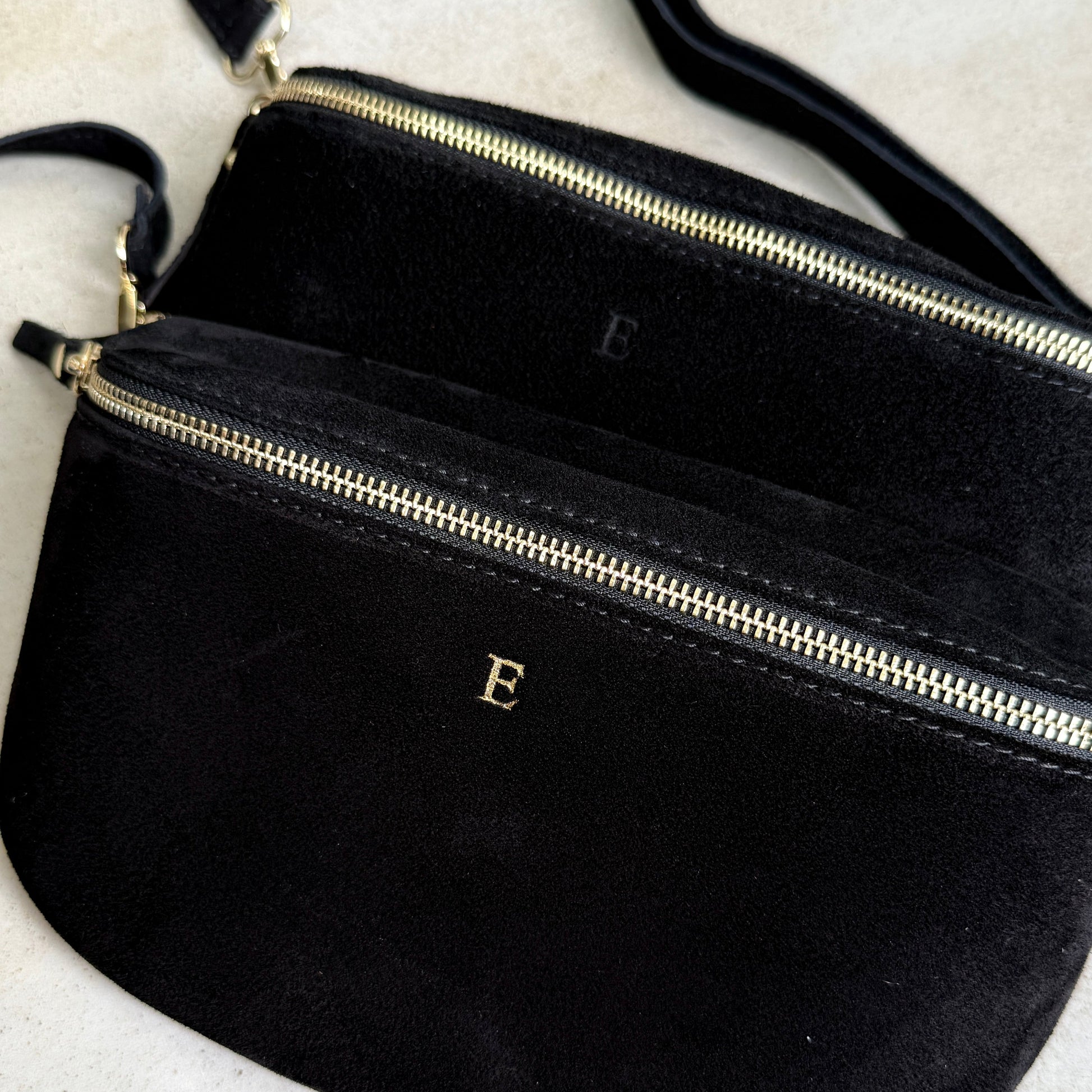 Black crossbody bag with a gold zipper and 'E' logo on a light gray background