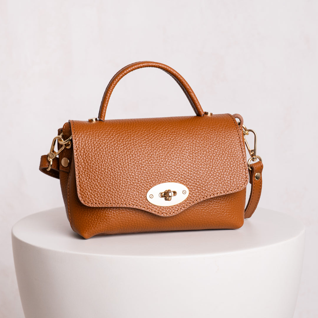 Brown leather handbag with gold accents on a white pedestal