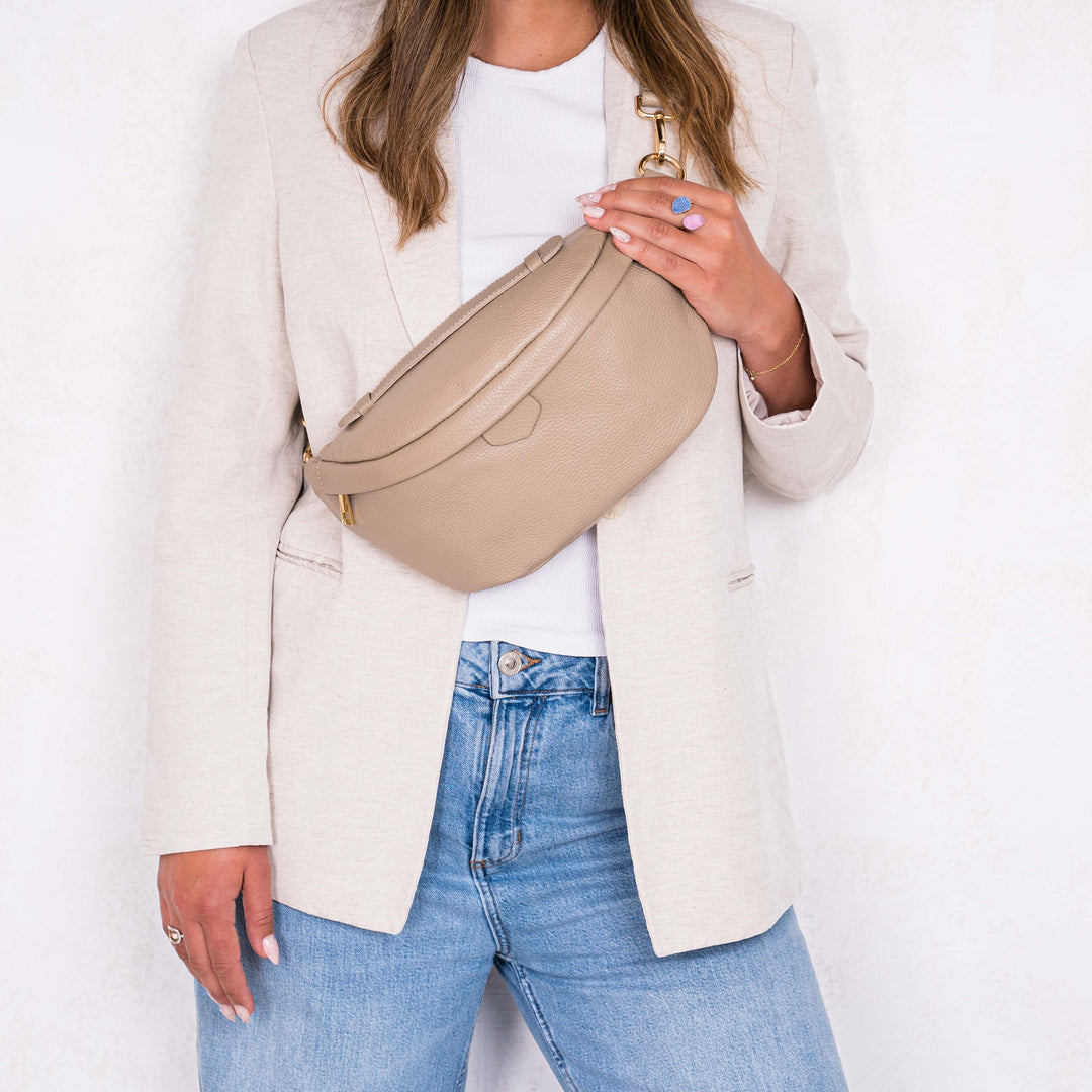 lady wearing cream jacket and jean holding a olivia and gray leather bumbag 