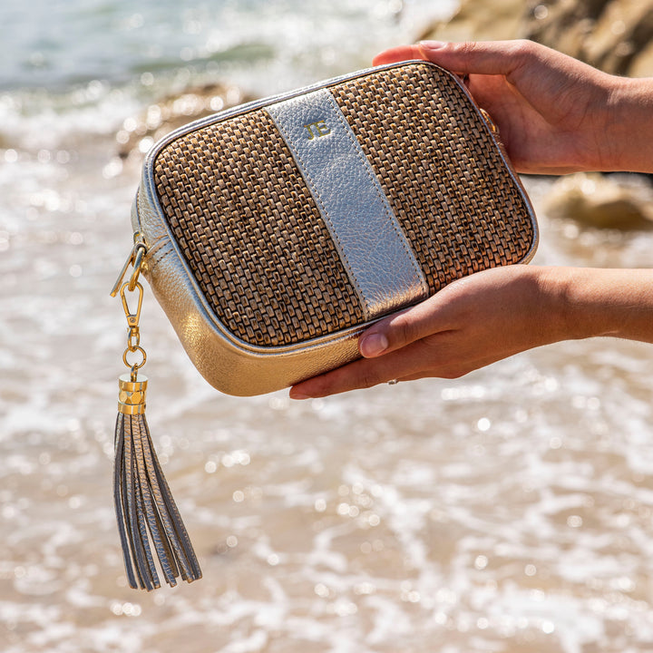 Hand holding a woven bag with a tassel by the ocean