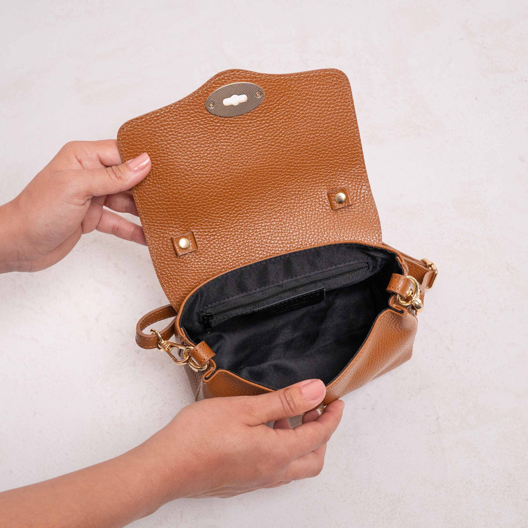 Brown leather handbag with gold accents held open by a hand on a light background