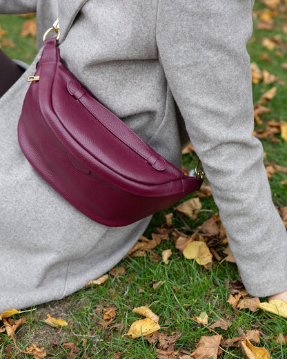 Person wearing a gray coat with a burgundy handbag on a grassy background with fallen leaves.