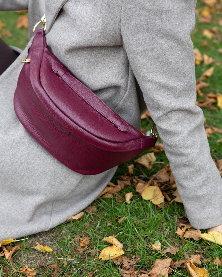 Person wearing a gray coat with a burgundy handbag on a grassy background with fallen leaves.